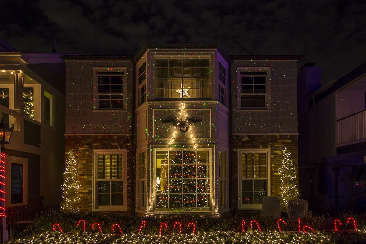 Large home decorated with laser dot lights, a lit star, and candy cane lawn decorations
